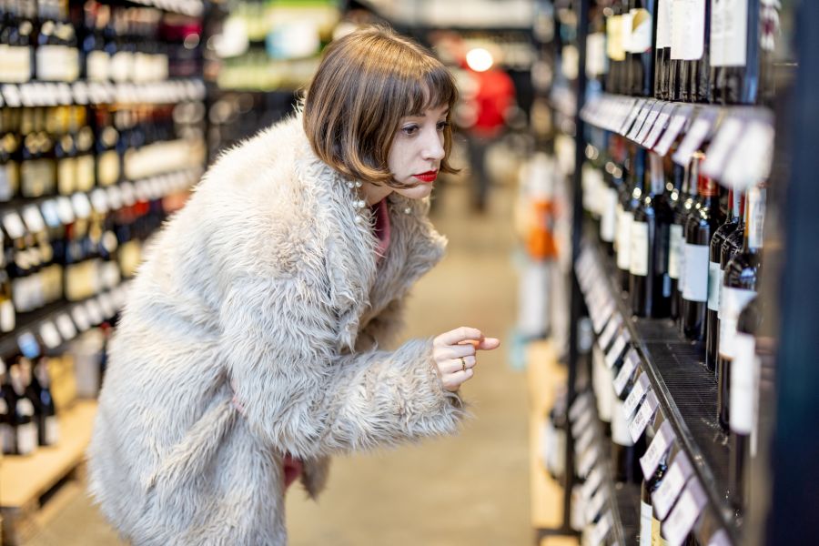 Frau sucht Wein aus einem Regal im Supermarkt aus